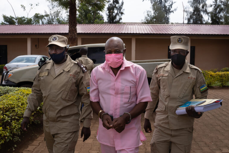 (FILES) In this file photograph taken on October 2, 2020, "Hotel Rwanda" hero Paul Rusesabagina (C) wears a pink prison inmate's uniform as he arrives at Nyarugenge Court of Justice in Kigali, flanked by guards of The Rwanda Correctional Service (RCS)